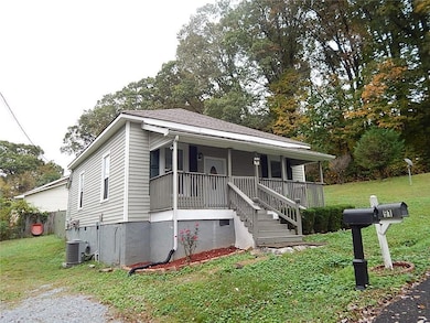Bungalow with a front yard, a porch, stairway, and view of wooded area