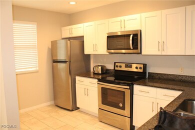 Kitchen featuring appliances with stainless steel finishes, white cabinets, light tile patterned floors, dark stone countertops, and recessed lighting