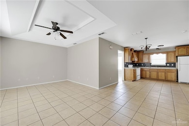Kitchen featuring freestanding refrigerator, range, a tray ceiling, light countertops, and a chandelier