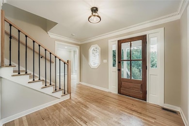 Foyer entrance featuring stairway, crown molding, and light wood-style flooring