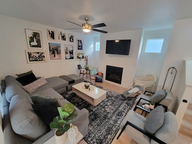 Living room featuring wood finished floors, a glass covered fireplace, plenty of natural light, and a ceiling fan
