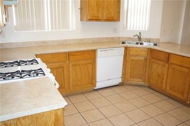 Kitchen featuring light tile patterned floors, light countertops, white appliances, and brown cabinets