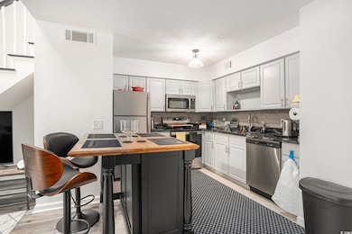 Kitchen featuring stainless steel appliances, backsplash, a textured ceiling, light wood-style flooring, and white cabinetry