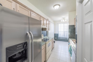 Kitchen with white appliances, light tile patterned floors, tile walls, light brown cabinetry, and ceiling fan