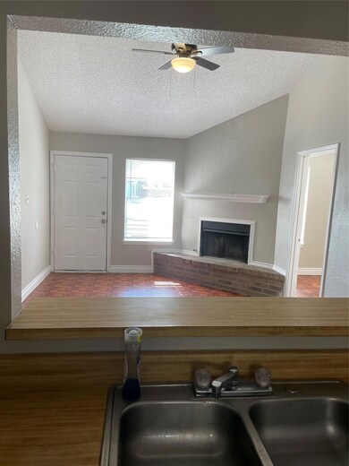 Living area with a textured ceiling, a brick fireplace, wood finished floors, a ceiling fan, and a textured wall