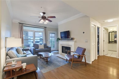 Living area featuring a tile fireplace, wood-finished floors, ceiling fan, and crown molding