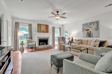 Living room featuring wood finished floors, crown molding, ceiling fan, and a fireplace