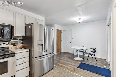 Kitchen with stainless steel appliances, tasteful backsplash, white cabinets, light wood-style floors, and light countertops