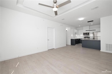 Unfurnished living room with a tray ceiling, visible vents, light wood-style flooring, and a ceiling fan