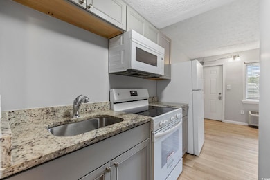 Kitchen featuring white appliances, a sink, a textured ceiling, gray cabinetry, and light wood-style floors
