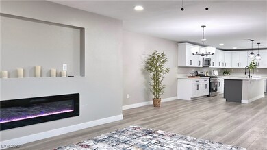 Living room featuring light wood-style flooring, a glass covered fireplace, recessed lighting, and a chandelier