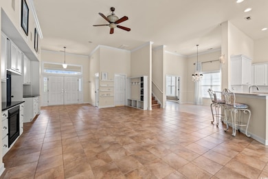 Living area featuring stairs, ornamental molding, a towering ceiling, a ceiling fan, and a chandelier