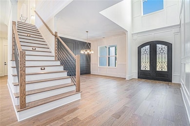 Foyer entrance featuring a decorative wall, a chandelier, stairs, light wood finished floors, and french doors