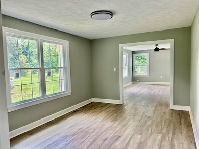 Spare room with light wood-type flooring, baseboards, a textured ceiling, and ceiling fan