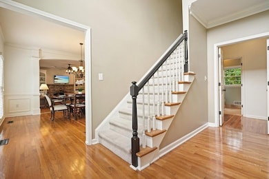 Staircase featuring wood finished floors, ornamental molding, a chandelier, and baseboards
