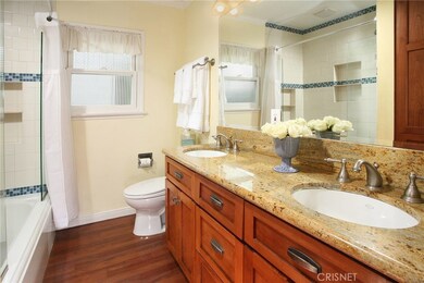 Sumptuous remodeled bathroom with state-of-the-art granite topped vanity with His and Her dual basins, large beveled glass dressing mirror, designer lighting, custom tiled shower/tub with decorative mosaic inlay, privacy window and wood flooring.