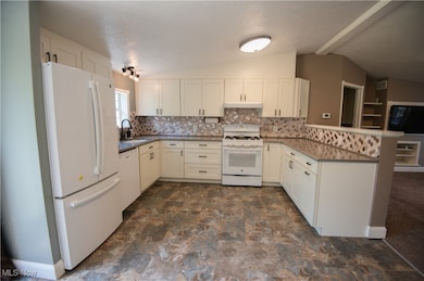 Kitchen featuring white appliances, a peninsula, decorative backsplash, and white cabinetry