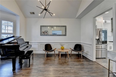 Living area with vaulted ceiling, a chandelier, wood finished floors, and a wainscoted wall