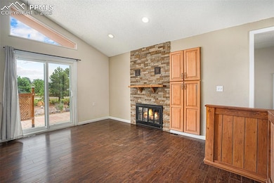 Unfurnished dining room with a textured ceiling, dark wood-style flooring, vaulted ceiling, and a stacked stone fireplace