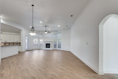Unfurnished living room with ceiling fan, ornamental molding, light wood-style floors, a glass covered fireplace, and recessed lighting