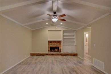 view of the large living room with lighted ceiling fan, fireplace and built in book case, hardwood tile floor and vaulted ceiling, fresh paint and texture.