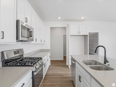 Kitchen with stainless steel appliances, white cabinets, recessed lighting, light wood-style flooring, and light stone counters