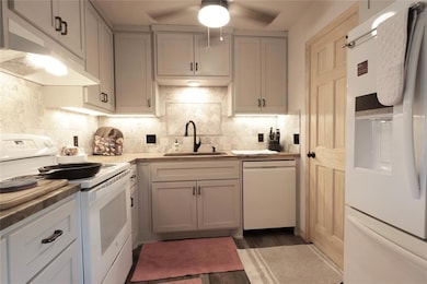 Kitchen featuring white appliances, under cabinet range hood, a ceiling fan, dark wood-style floors, and gray cabinets
