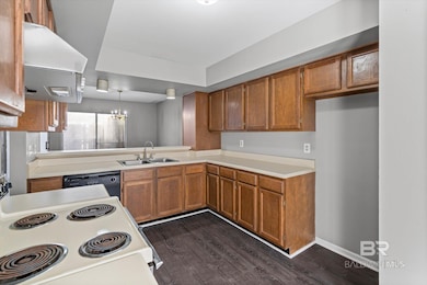 Kitchen with brown cabinets, a chandelier, electric stove, exhaust hood, and dark wood-type flooring