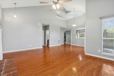 Living and Dining room areas with high vaulted ceiling, a brick fireplace, hardwood flooring, and ceiling fan.