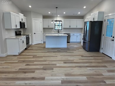 Kitchen featuring appliances with stainless steel finishes, pendant lighting, recessed lighting, a kitchen island, and light wood-style flooring