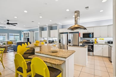 Kitchen featuring appliances with stainless steel finishes, a kitchen island, light tile patterned floors, a ceiling fan, and ornamental molding
