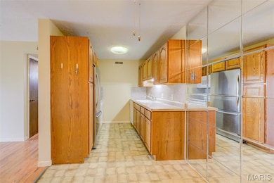 Kitchen with light countertops, freestanding refrigerator, brown cabinets, a textured ceiling, and backsplash