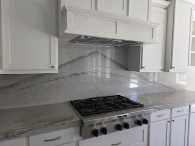 Kitchen with custom exhaust hood, white cabinetry, stainless steel gas stovetop, and light stone counters