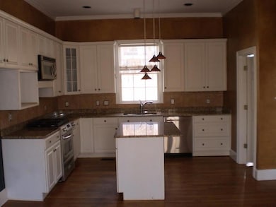 Kitchen with stainless steel appliances, dark wood-style flooring, ornamental molding, glass insert cabinets, and white cabinetry