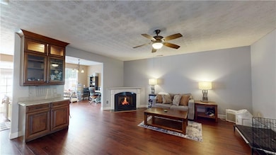 Living area featuring dark wood-style flooring, a ceiling fan, a textured ceiling, and a fireplace with flush hearth