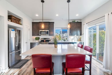 Kitchen featuring a kitchen bar, stainless steel appliances, dark brown cabinets, decorative backsplash, and hanging light fixtures