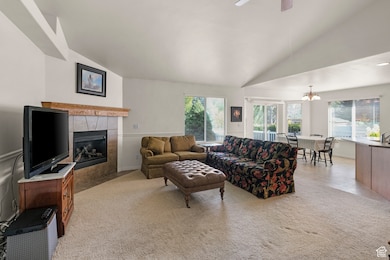 Living area with lofted ceiling, a tile fireplace, light colored carpet, and a ceiling fan