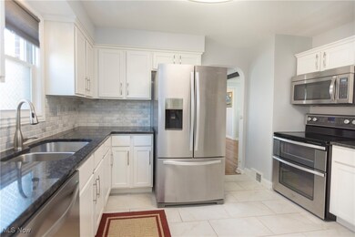 Kitchen with tasteful backsplash, stainless steel appliances, sink, white cabinetry, and dark stone countertops