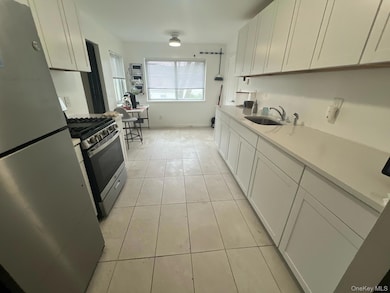 Kitchen featuring white cabinetry, appliances with stainless steel finishes, light tile patterned floors, and light stone countertops