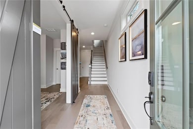 Entryway featuring recessed lighting, light wood-type flooring, baseboards, a barn door, and stairs
