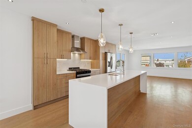 Kitchen with modern cabinets, tasteful backsplash, hanging light fixtures, black gas range oven, and wall chimney exhaust hood