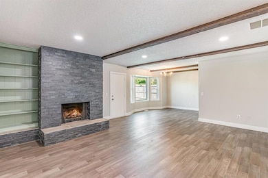 Unfurnished living room with a textured ceiling, a stone fireplace, a chandelier, wood finished floors, and beamed ceiling
