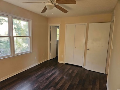 Unfurnished bedroom featuring multiple windows, dark wood finished floors, a closet, a textured ceiling, and ceiling fan