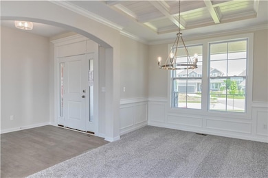 Carpeted foyer entrance featuring arched walkways, a chandelier, beamed ceiling, ornamental molding, and a wainscoted wall