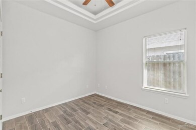 Unfurnished room featuring a ceiling fan, wood finish floors, baseboards, and a tray ceiling