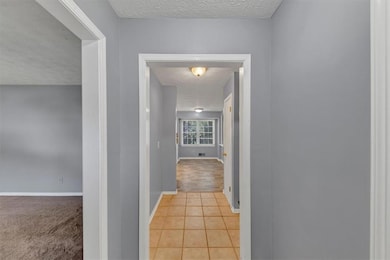 Hallway with a textured ceiling and light tile patterned floors