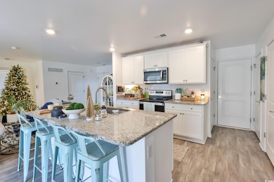 Kitchen with light wood-type flooring, white cabinets, a breakfast bar, stainless steel appliances, and light stone countertops