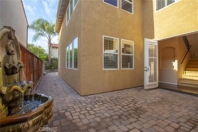 French doors open to a court yard of brick pavers, accented by the fountain.   There are 4 Palm trees in the back. In the background is the front staircase.