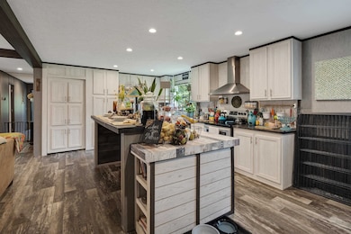 Kitchen featuring dark wood-type flooring, wall chimney range hood, recessed lighting, stainless steel electric range oven, and a kitchen island