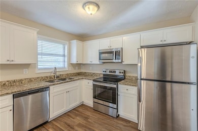 Kitchen featuring white cabinets, appliances with stainless steel finishes, dark wood-type flooring, light stone countertops, and a sink